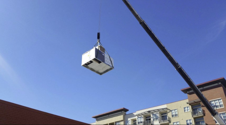 A crane lifting an air con unit on to the top of an apartment.